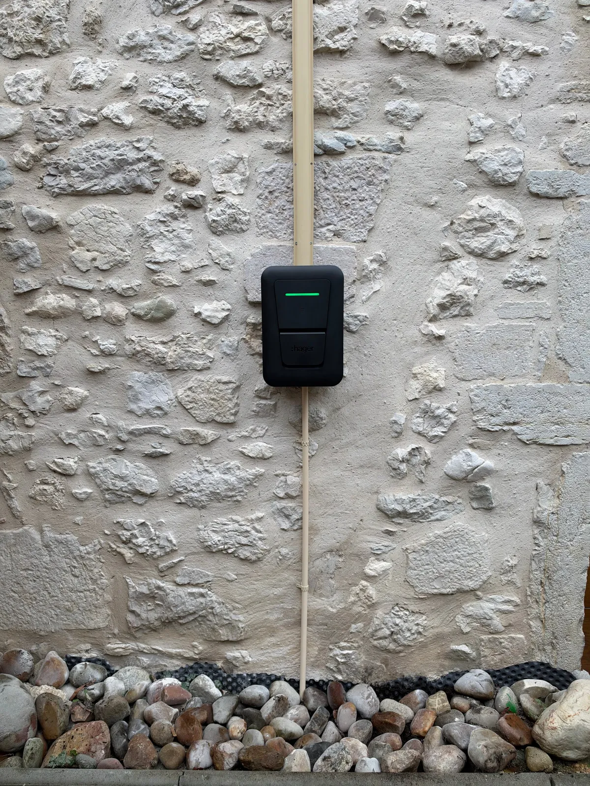 Borne de recharge Hager Witty One 11 kW sur un mur en pierre, câble masqué par un profilé de protection oméga couleur pierre, Ceyzérieu (01)