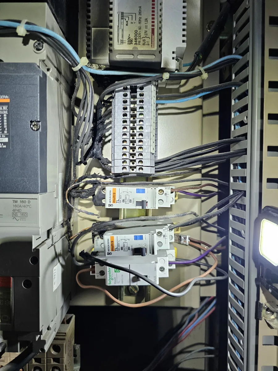 Câblage carbonisé et borniers fondus après départ de feu dans une armoire électrique à Belley