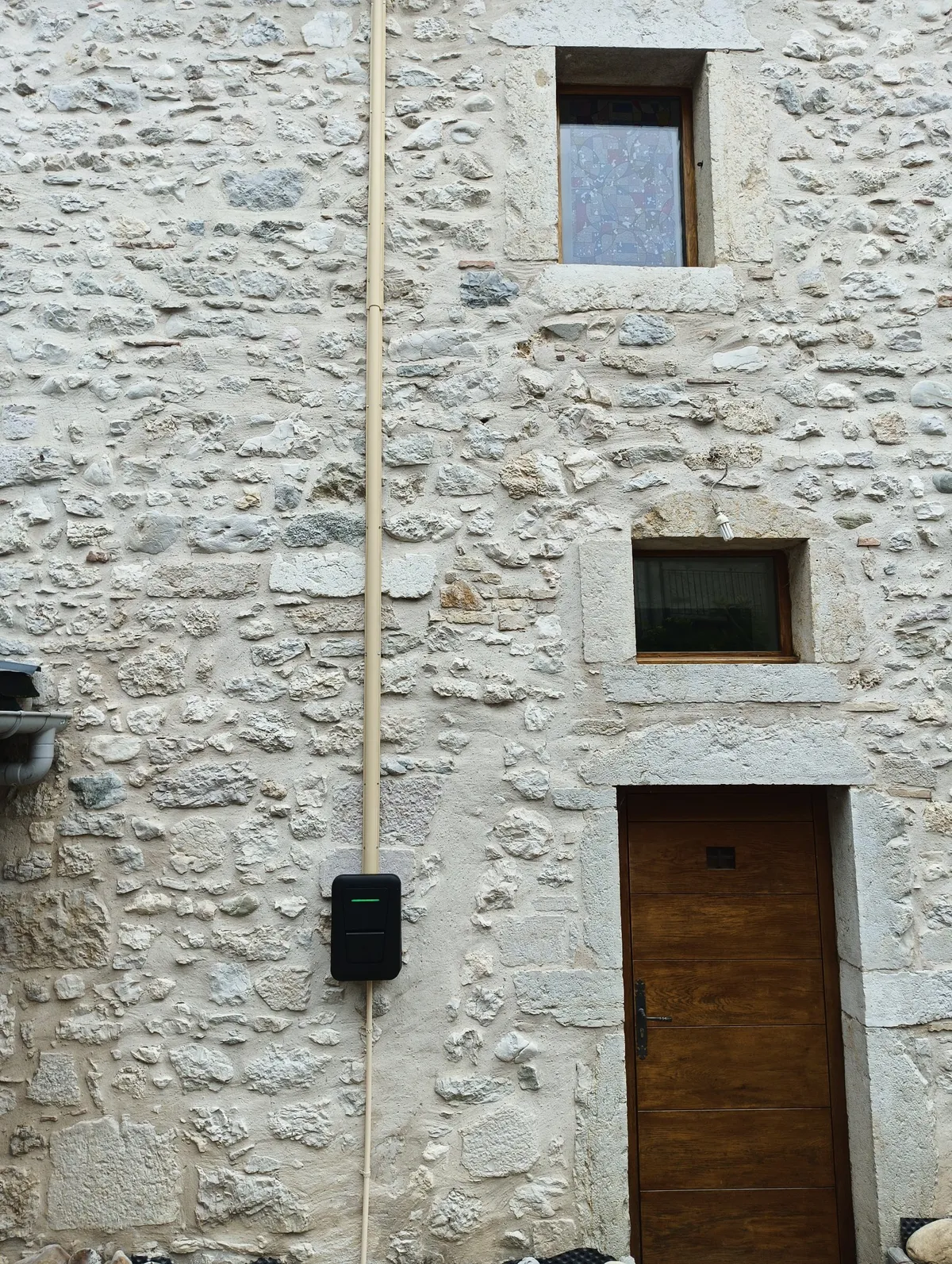 Façade en pierre avec une borne de recharge Hager Witty One 11 kW et un profilé oméga ton pierre qui monte le long du mur, Ceyzérieu (01)